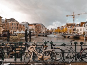 Uitzicht op een van de kanalen in Leiden met geparkeerde fietsen op de brug op de voorgrond. Foto afkomstig van Unsplash gemaakt door Jose Zuniga
