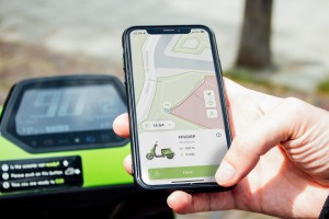 Een smartphone waarop een persoon via een app een deelscooter aan het reserveren is