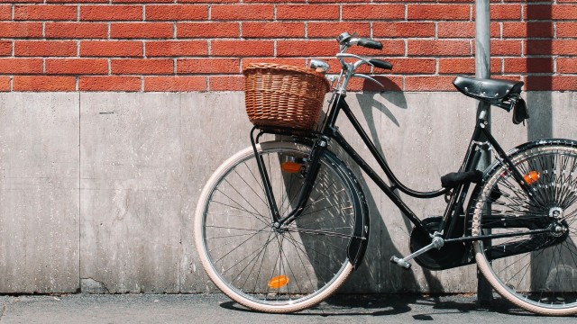 Een fiets met rietenmand die geparkeerd staat tegen een muur